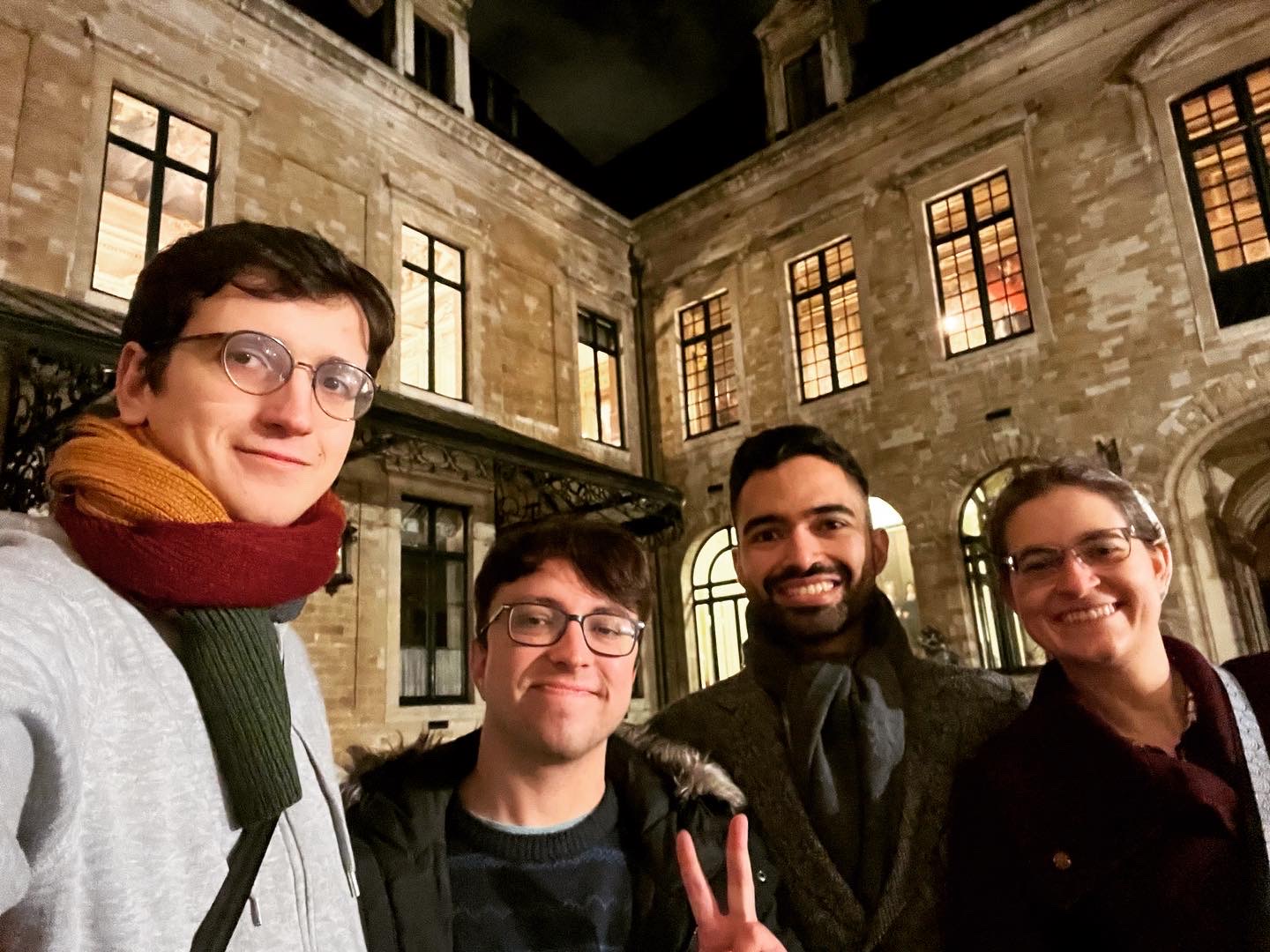 4 people in front of an old stone building: a tall, bespectacled man with a colorful scarf, a shorter man giving a peace sign and looking ready to laugh, a taller man with great hair and a fashionable scarf and wool coat, and me with my glasses and dark red wool coat /images/2023/diego_pablo_nelson_maco.jpg