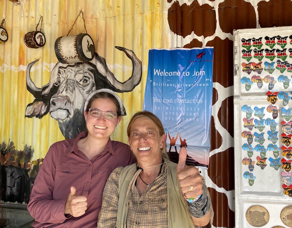 Two people give thumbs up to the camera. I’m in a mauve shirt with a white headcovering. Ellerie is in lots of beige. Behind us on the wall is a painting of a gnu. /images/2023/maco_ellerie.jpg
